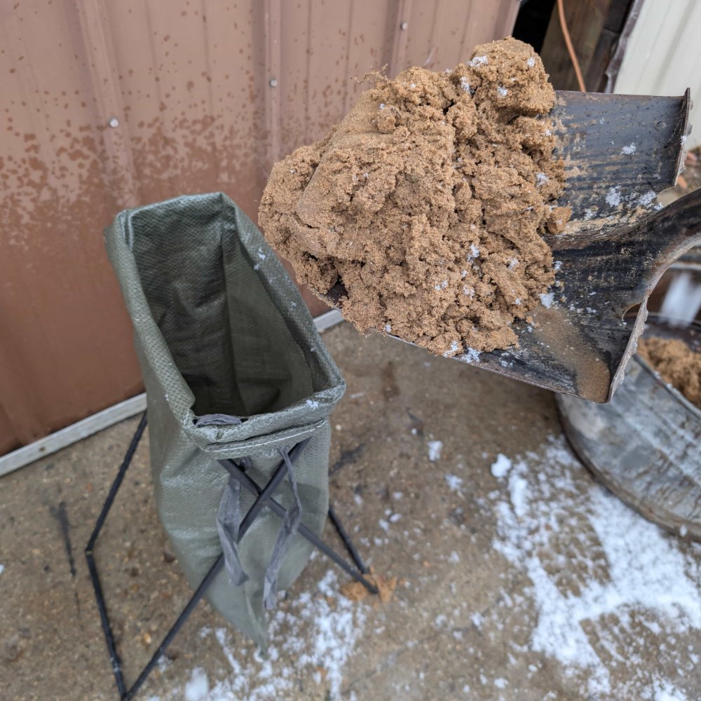 Shovelling sand into a bag held open by the stand
